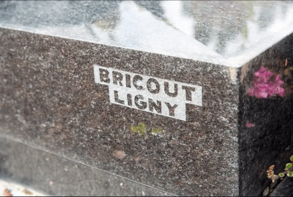 Détail de la signature Pompes Funèbres Bricout Ligny gravée sur le socle d'un monument funéraire.