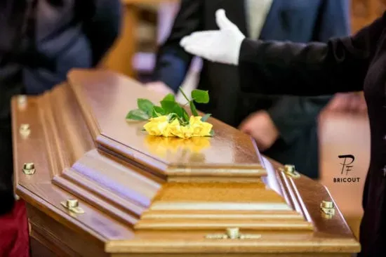 Cercueil en bois verni surmonté de fleurs jaunes lors d’un hommage funéraire.