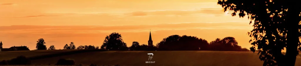 Paysage campagnard au coucher du soleil avec clocher d'église en arrière-plan.