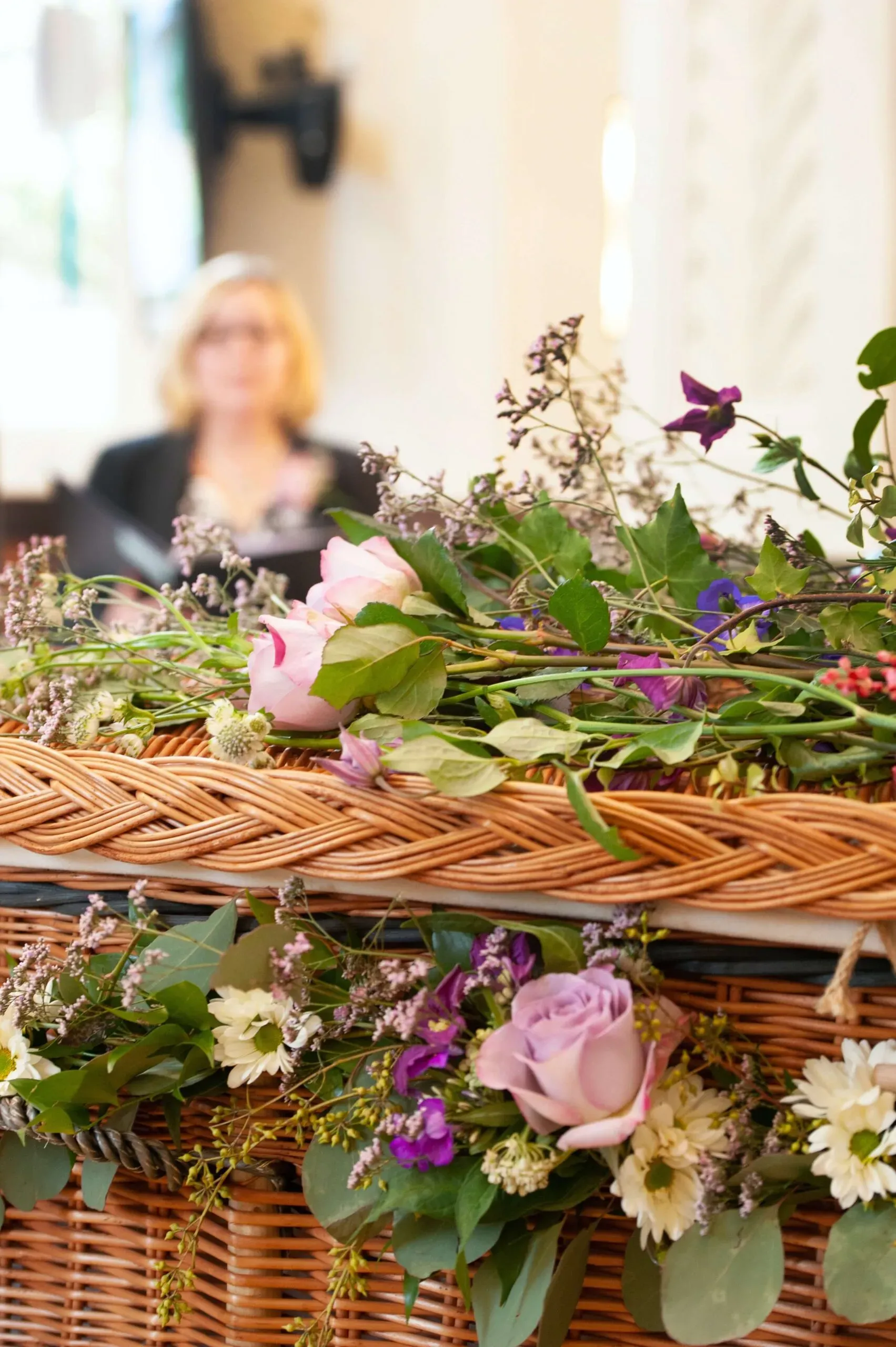 Cercueil en osier tressé orné de roses fraîches et fleurs champêtres lors d'une cérémonie.