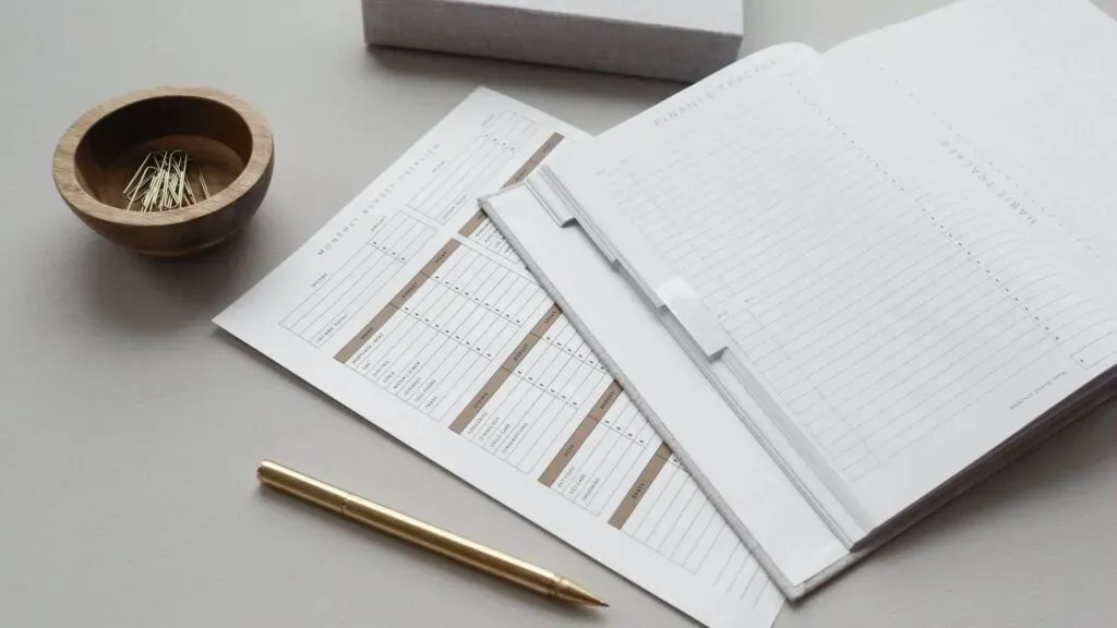 Documents d'organisation administrative et suivi de budget posés sur une table avec un stylo doré.