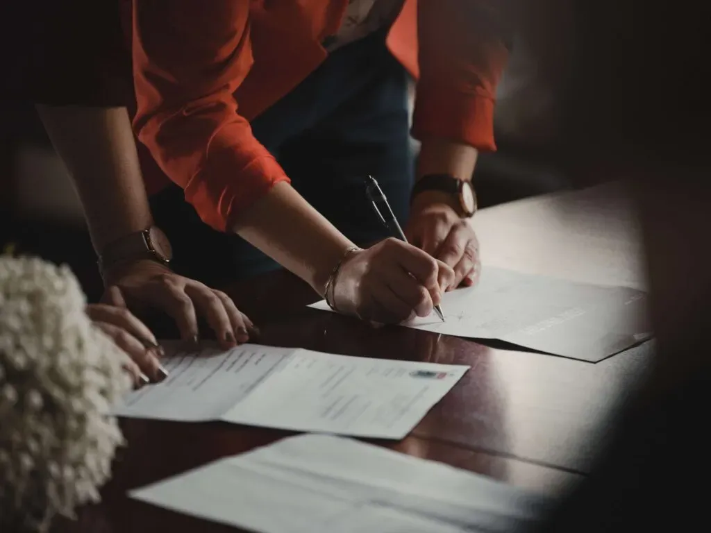 Personne signant des documents administratifs ou un contrat de prévoyance sur une table en bois.
